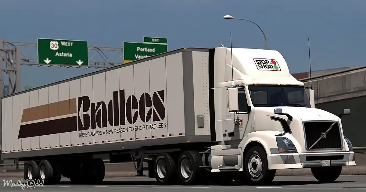 A white semi-truck with "Bradlees" branding drives on a highway under a sign for Route 30 West to Astoria.