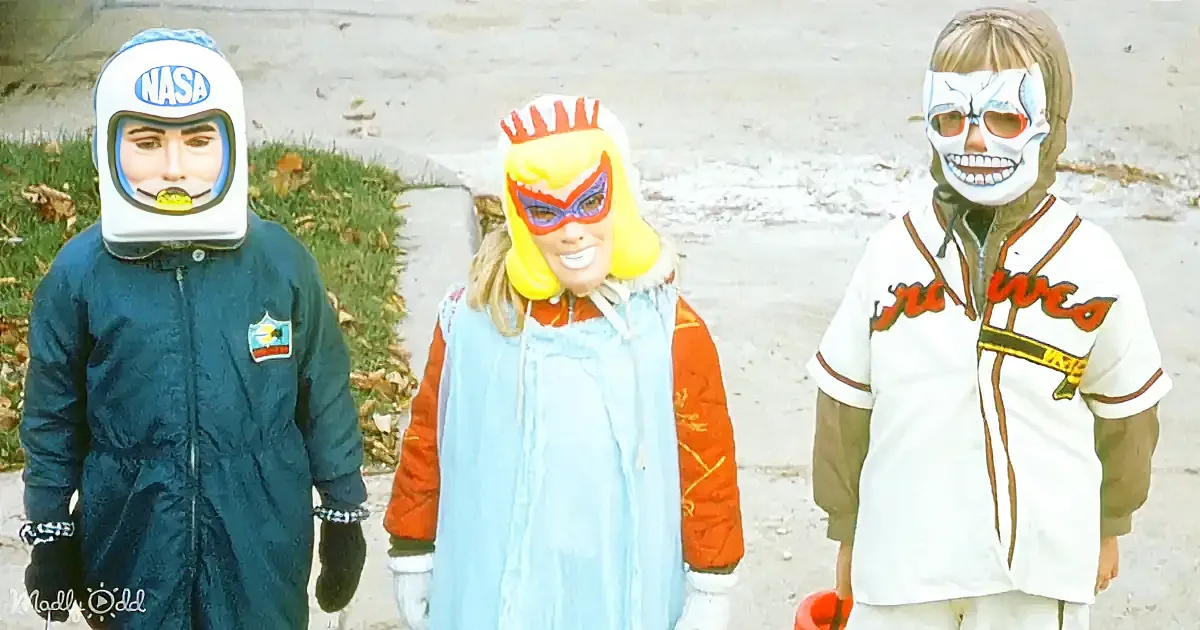 Three children in costumes, one in NASA suit, another in superhero, and the third in skeleton makeup, stand outdoors.