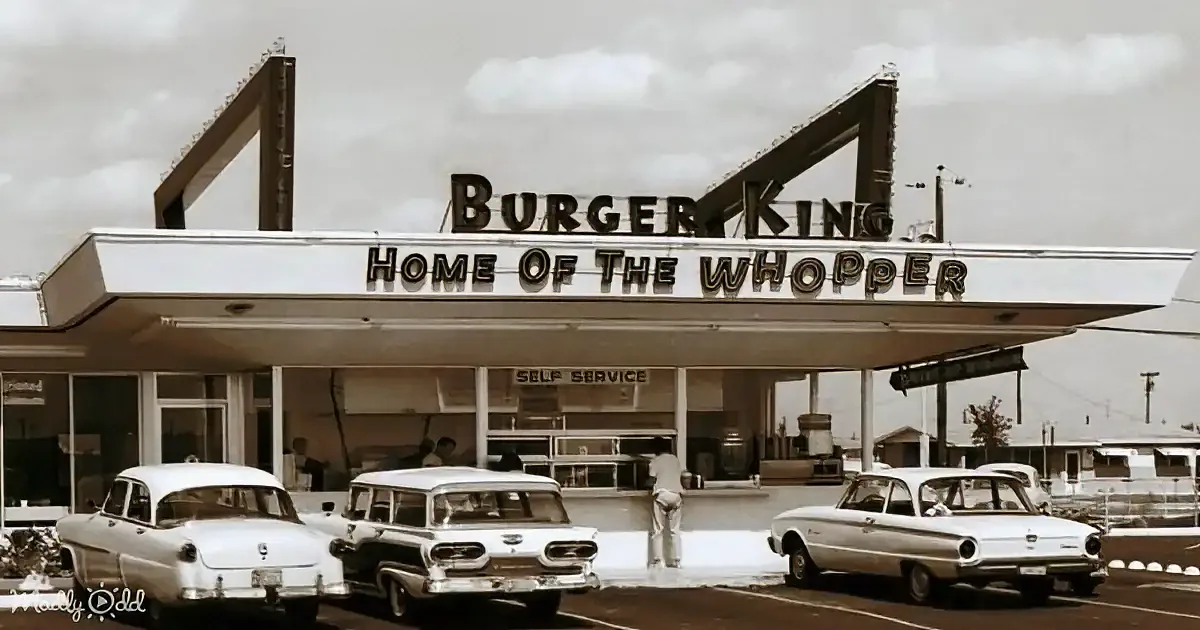 A vintage Burger King restaurant with cars parked in front, featuring the iconic "Home of the Whopper" sign.