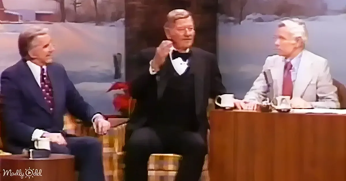 Three men in formal attire are seated, one gesturing, in a studio setting with a snowy backdrop.