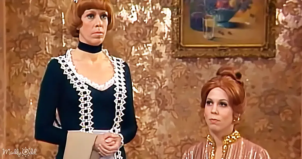 A woman in a dark blue dress with white trim stands, holding a folder, while another woman in a gold dress with a pearl...