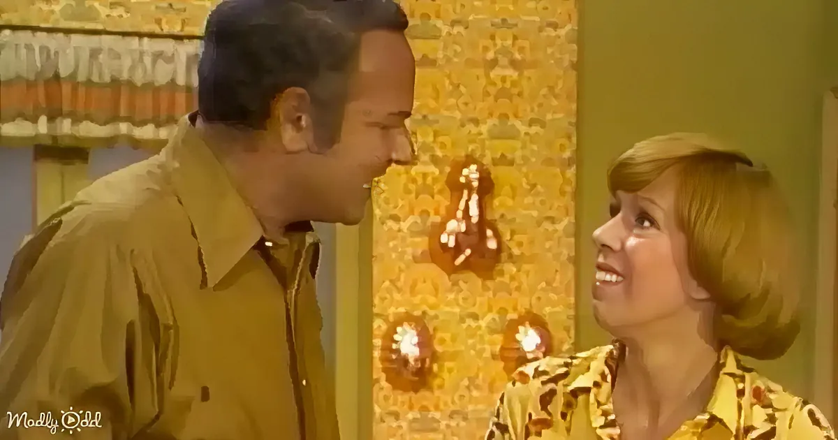 A man in a tan shirt leans towards a woman in a yellow floral shirt, both smiling in a room with yellow wallpaper and...