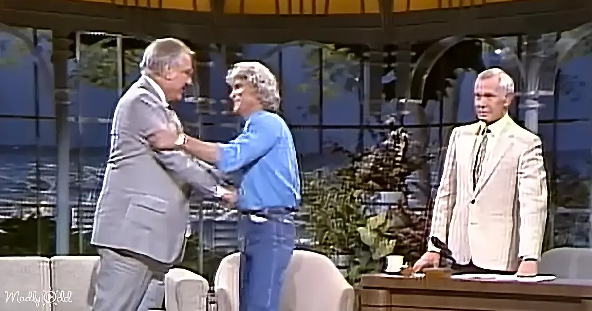 A man in a suit is playfully interacting with another man in casual attire on a talk show set.