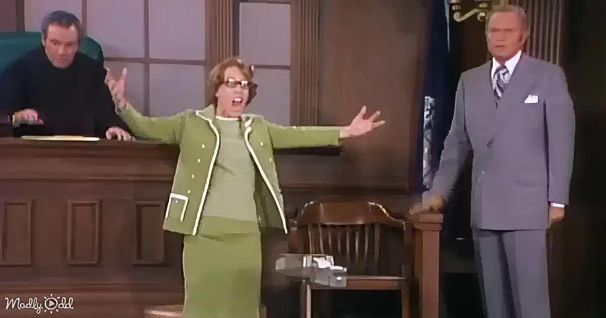 A woman in a green suit stands with arms outstretched in a courtroom setting.
