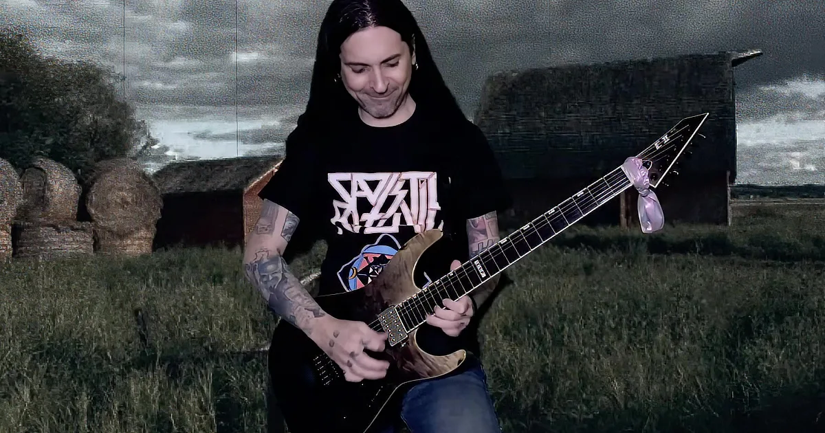 A guitarist with tattoos plays a guitar, wearing a black shirt and a hat, with sparks in the background.