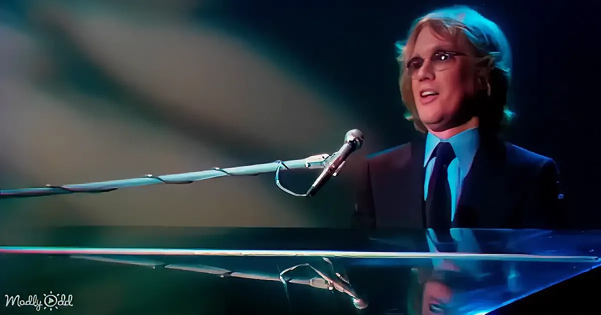 A man in a suit and tie sings into a microphone while playing a piano.