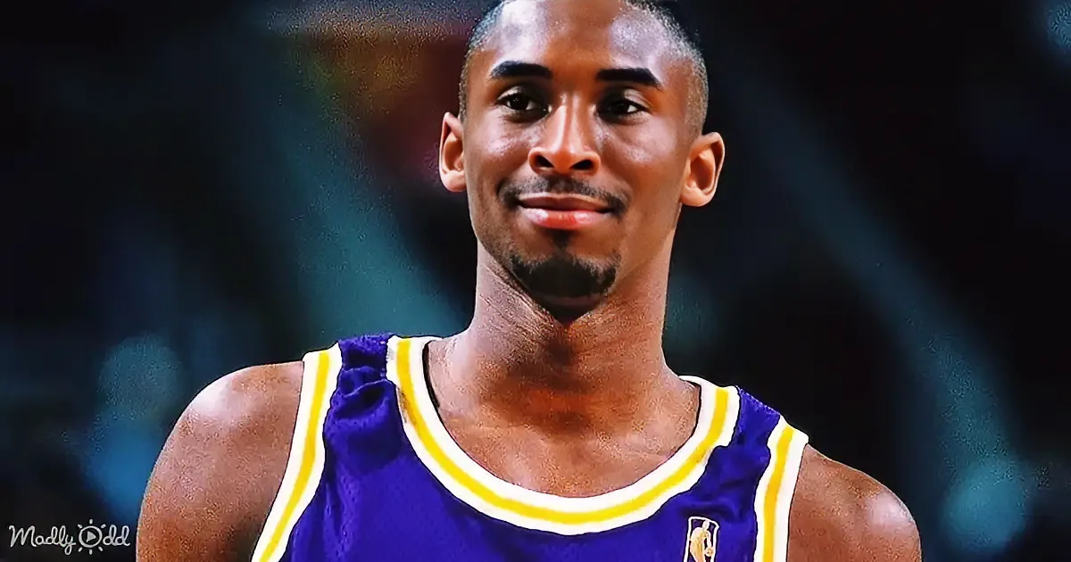 A basketball player in a purple jersey with yellow stripes smiles while wearing a mustache and goatee.