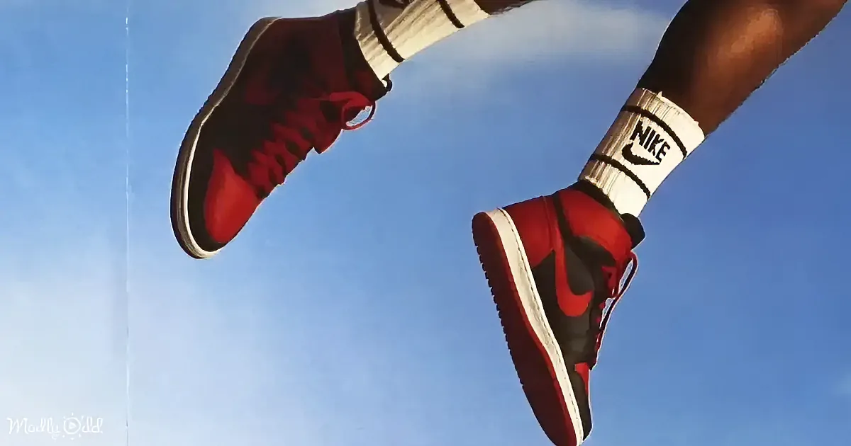 A person wearing red and black Nike sneakers and white socks is mid-air against a blue sky.