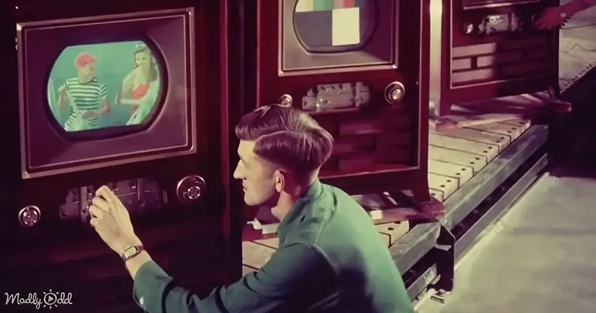 A man in a green shirt operates a vintage television set, with a woman in a red dress on the screen.