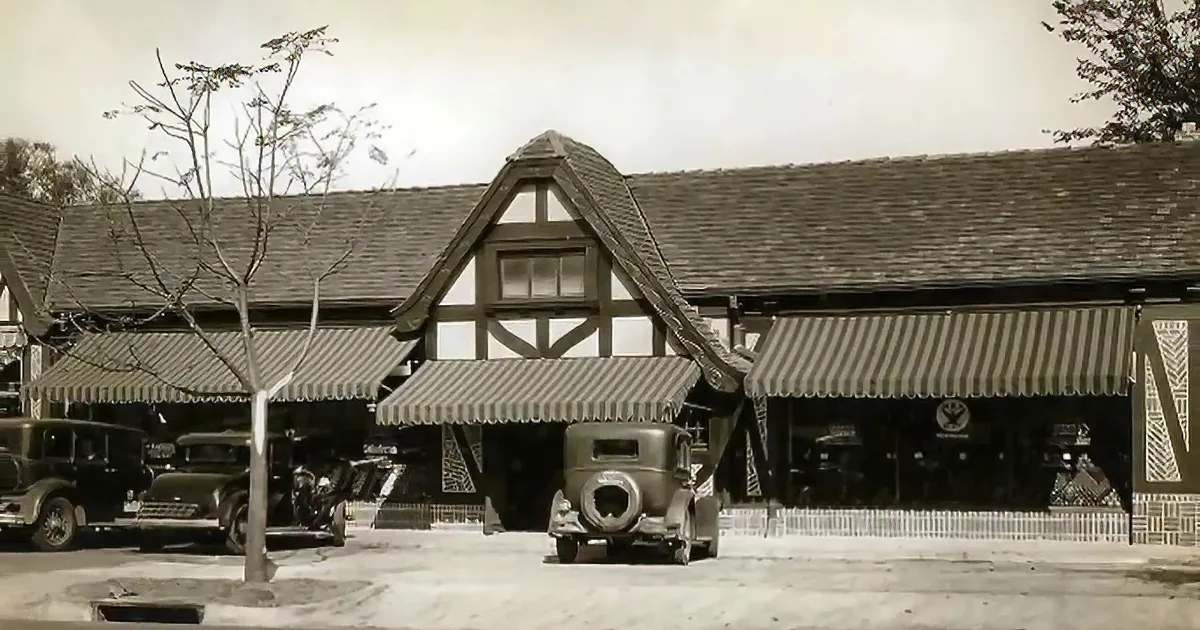 Vintage cars parked in front of a "Jitney Jungle" supermarket with retro signage and advertisements.