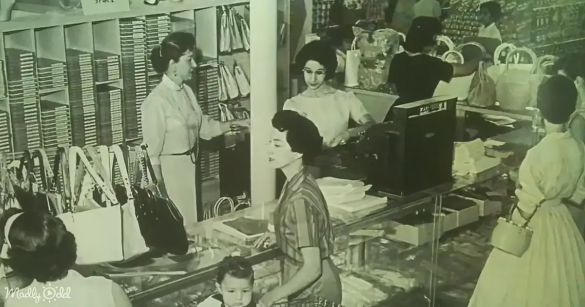 A woman in a striped shirt stands at a counter, surrounded by customers and merchandise, in a bustling store.