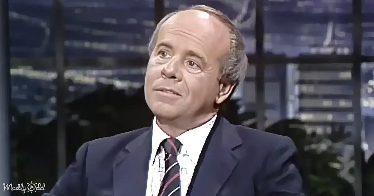 A man in a suit and tie, seated, looking to the side, with a cityscape in the background.