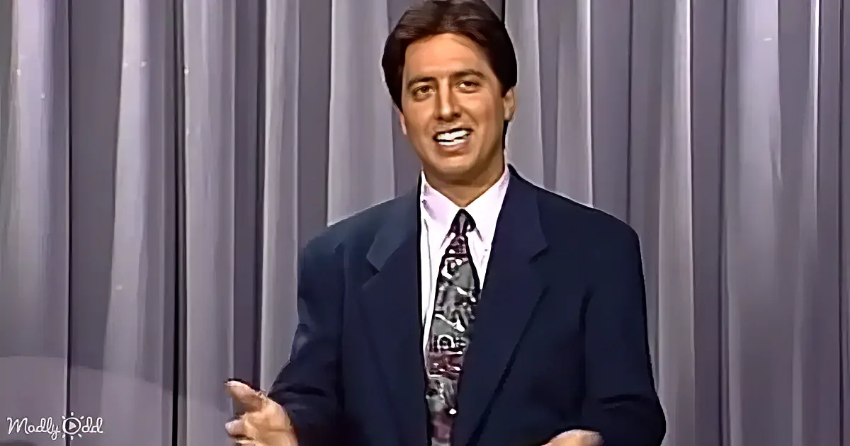 A man in a suit and tie is smiling and gesturing with his hand.