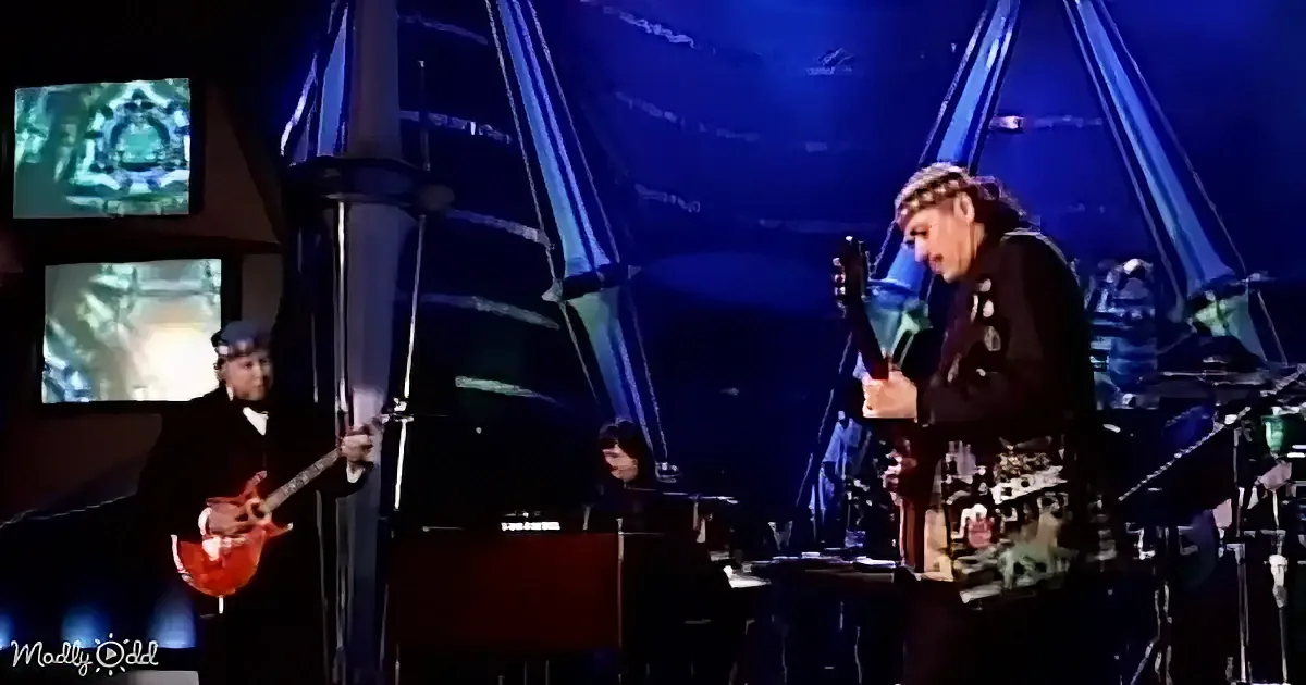 A musician in a black outfit with a headband is singing passionately on stage.