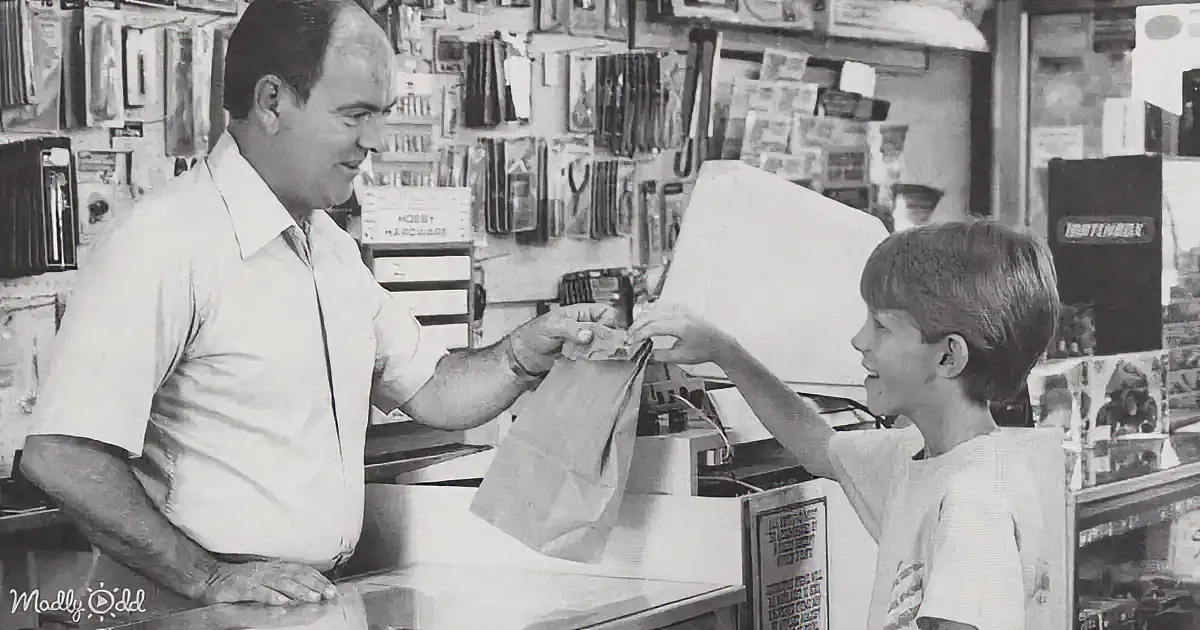 A man and a boy smile as the man hands the boy a bag in a store.