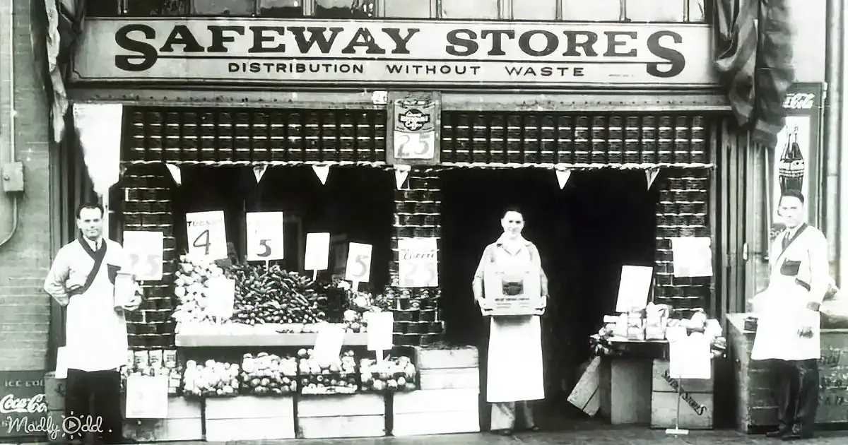 Three people in aprons stand in front of a Safeway Stores storefront with produce and signs displaying prices.