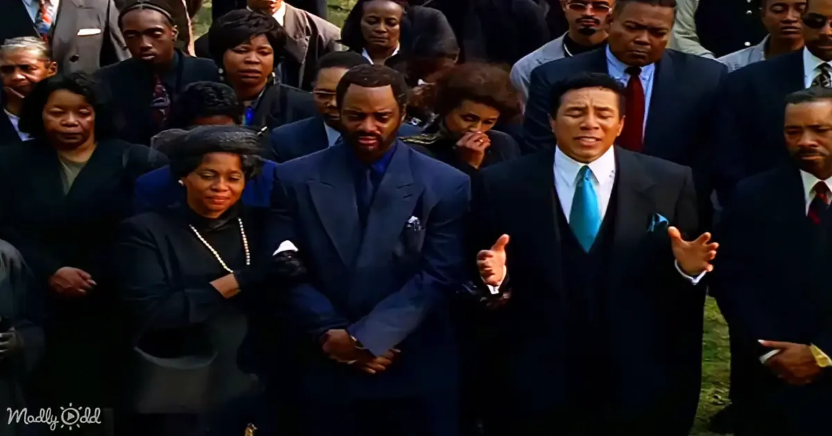 A man in a suit gestures passionately while standing in front of a crowd at a solemn event.