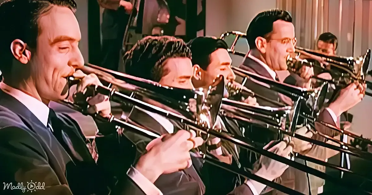 A group of musicians in suits play trombones in a line, with one prominently in the foreground.