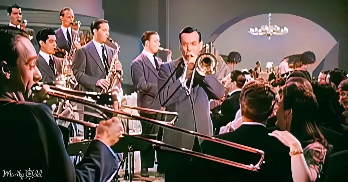 A man in a suit plays a trumpet in front of a jazz band and dancing crowd.