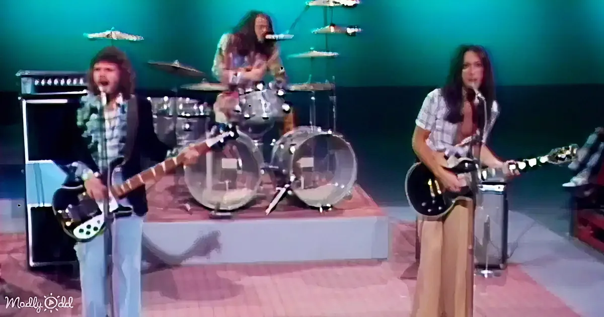 A person with long dark hair sings into a microphone against a blurred background.