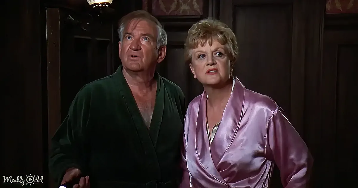 A man and woman in robes stand together, looking surprised or concerned in a dimly lit room.