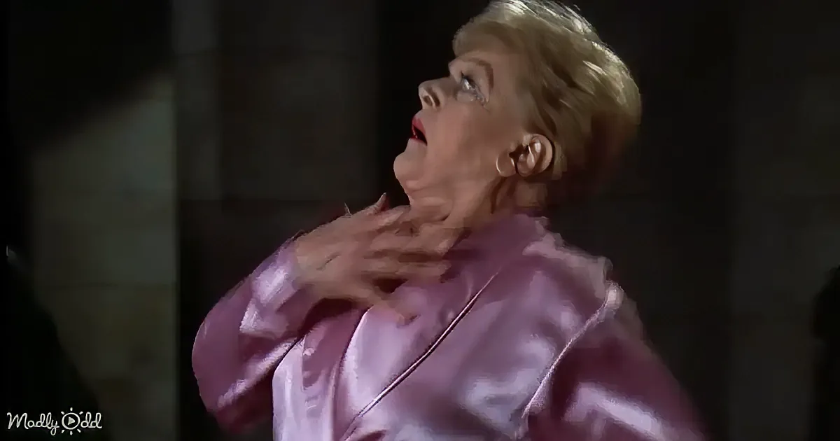 A woman in a pink satin robe is惊恐地伸手触摸她的脖子。