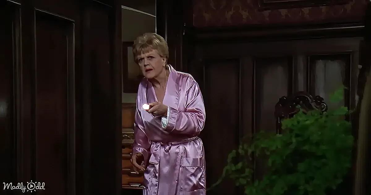 A woman in a purple robe stands in a room, holding a small object, with a wooden door and greenery in the background.