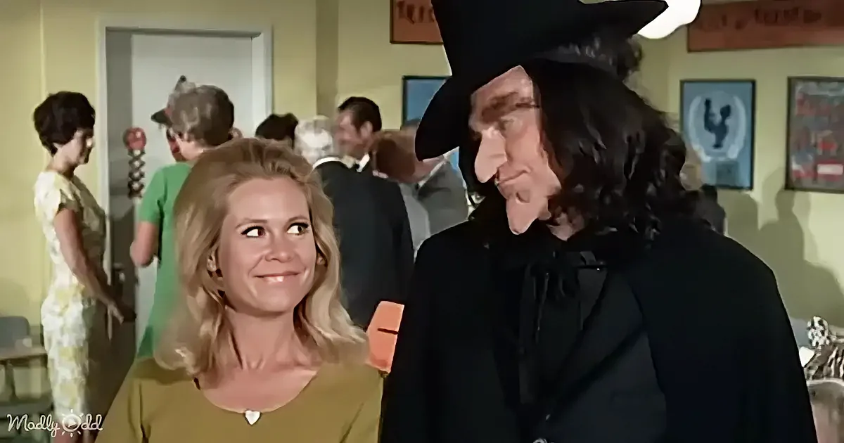 A woman in a green dress smiles at a man in a black suit and hat in a lively room.