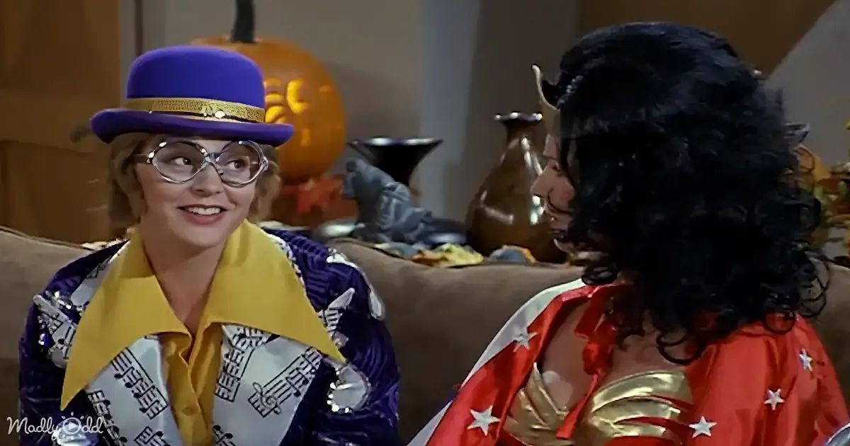 A woman in a purple hat and yellow scarf smiles at another woman in a red and gold costume.