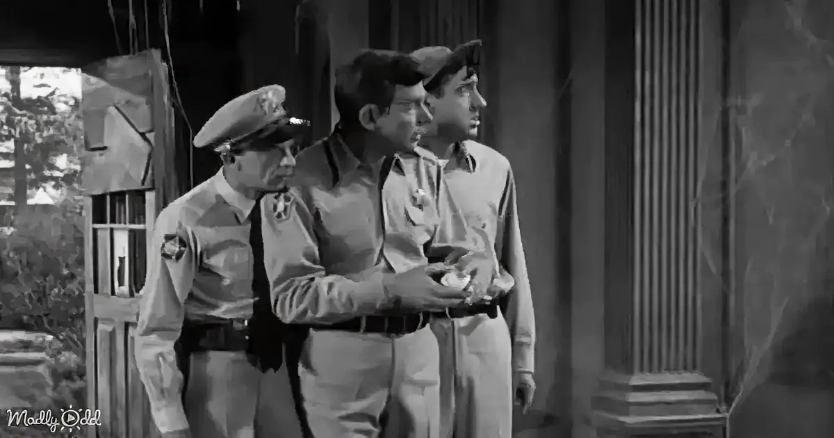 A man in a uniform holds another man's arm while a third man looks on, all in a dimly lit setting.