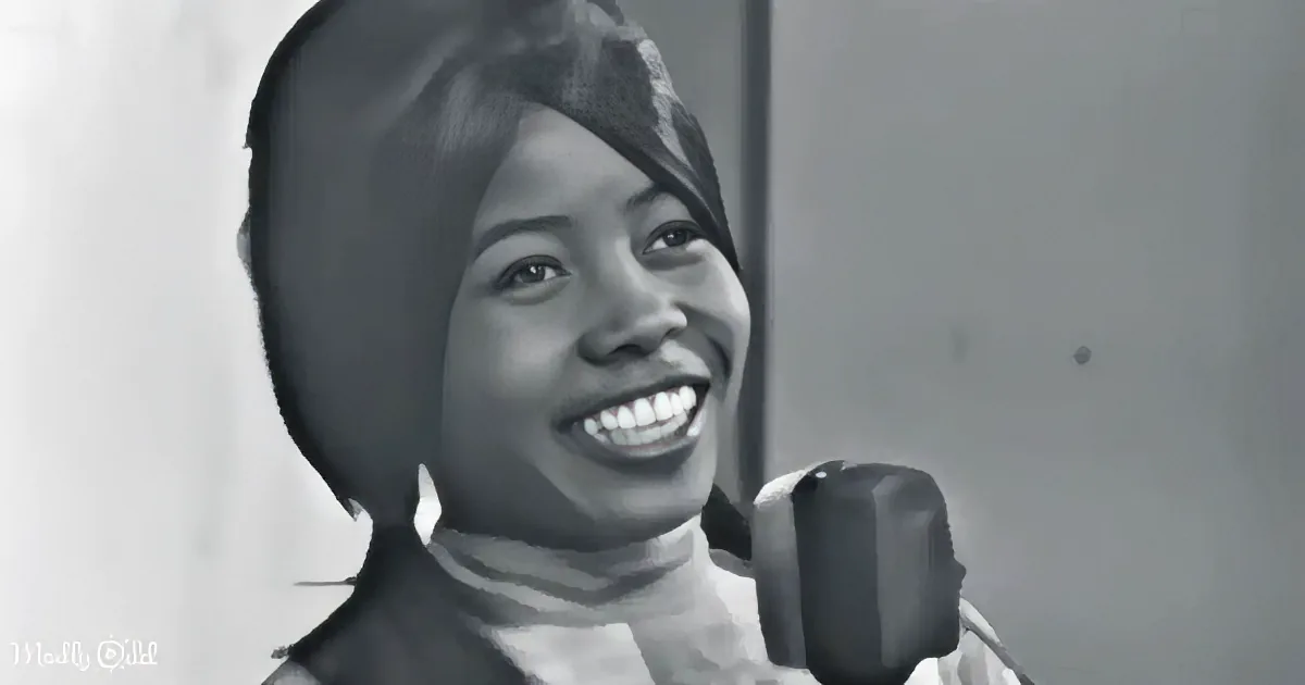A smiling woman with a microphone, wearing a dark top, in a black-and-white image.