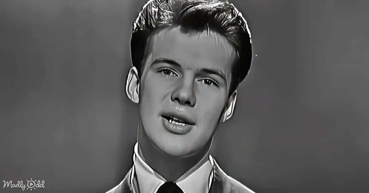 A man with short, styled hair, wearing a suit and tie, is shown in a black and white portrait.