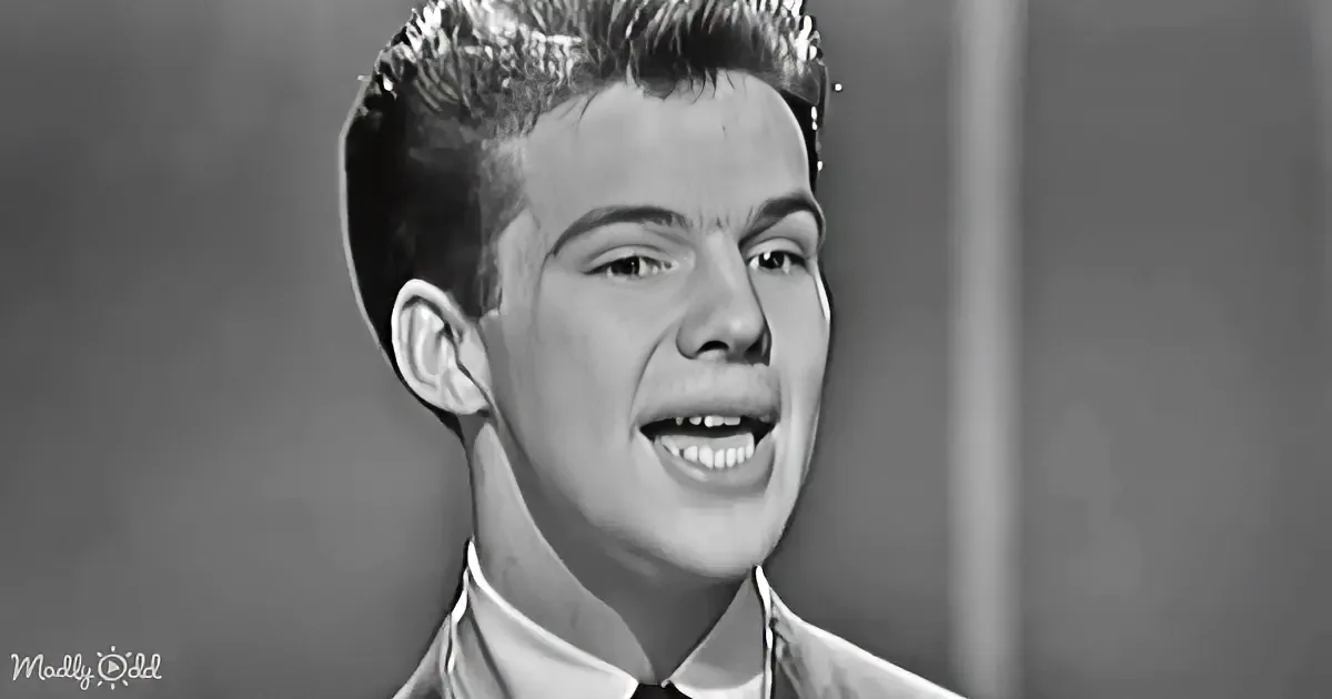 A young man with a quizzical expression, wearing a collared shirt, is the main subject of this black-and-white image.