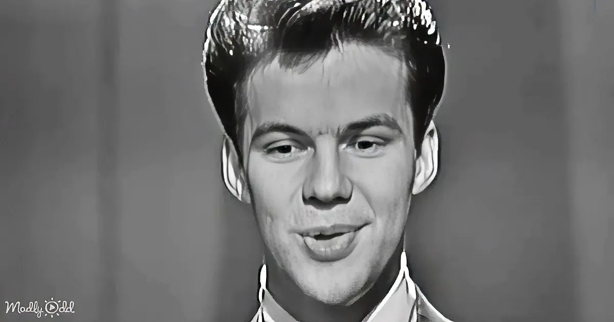 A young man with short, styled hair and a slight smile, wearing a collared shirt, is the main subject of this...