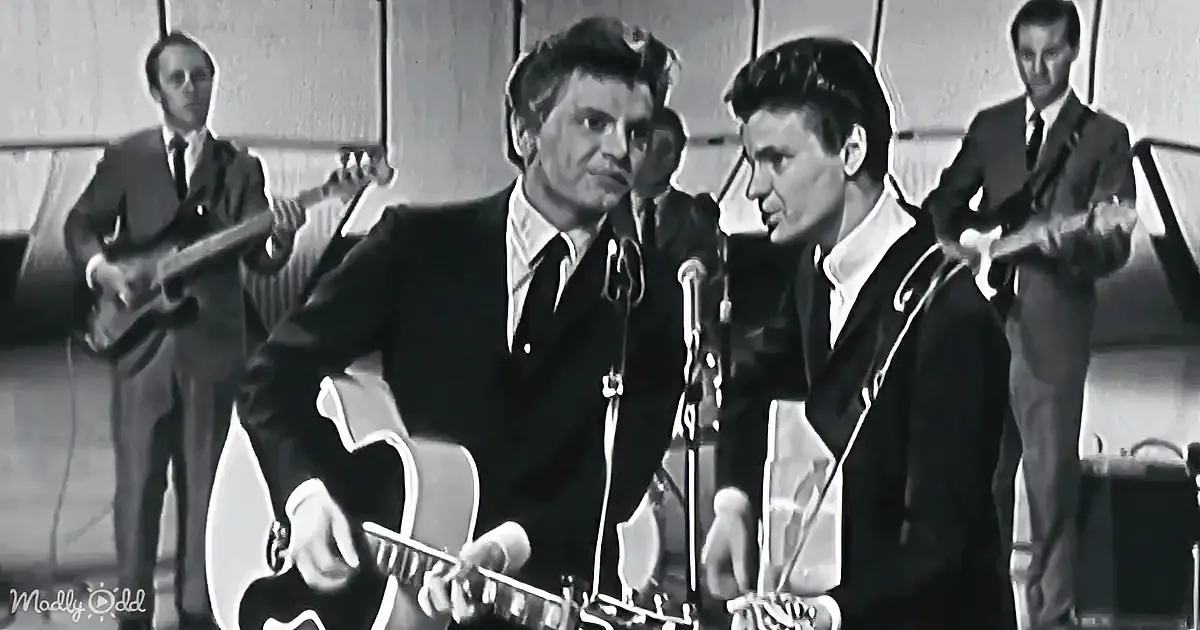 A man in a suit plays guitar on stage, surrounded by other musicians.