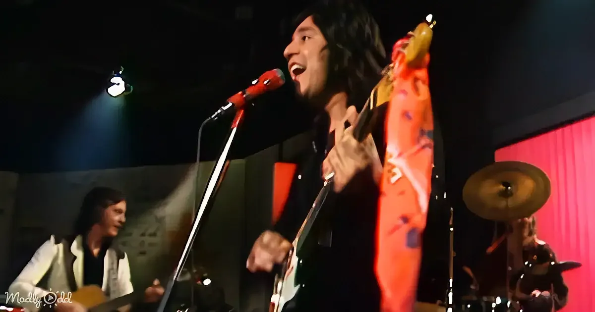 A guitarist passionately plays a vibrant orange guitar on stage, singing into a microphone.