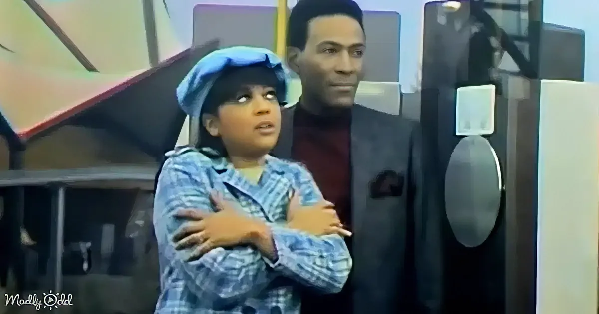 A person in a blue plaid shirt and blue hat stands with arms crossed, looking up, while another person in a suit stands...