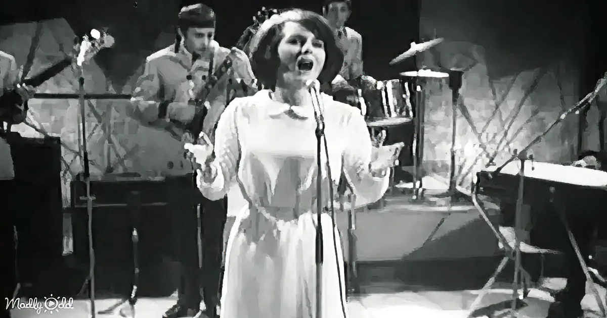 A woman in a white dress sings passionately on stage with a band behind her.