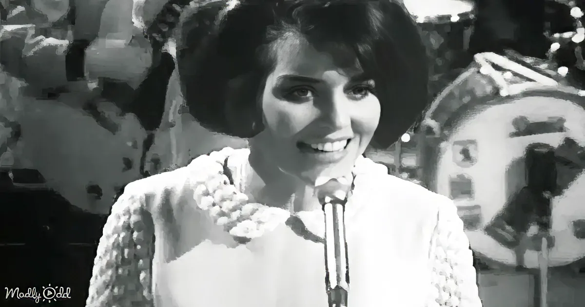 A woman in a white dress smiles while singing into a microphone, with a band in the background.