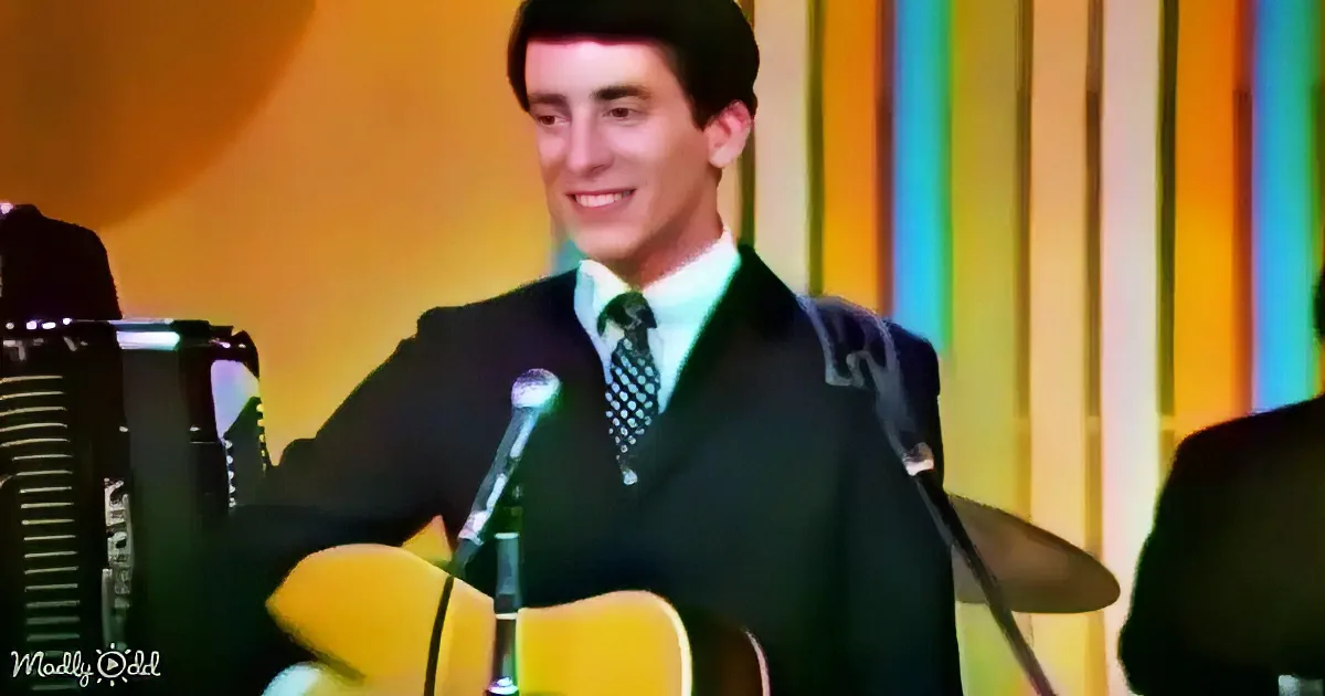 A man in a suit and tie smiles while playing a yellow guitar on stage.