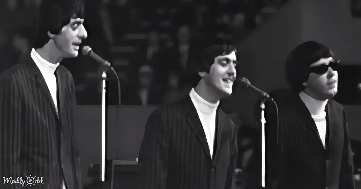 Three men in suits sing into microphones, wearing white shirts, in a black-and-white image.