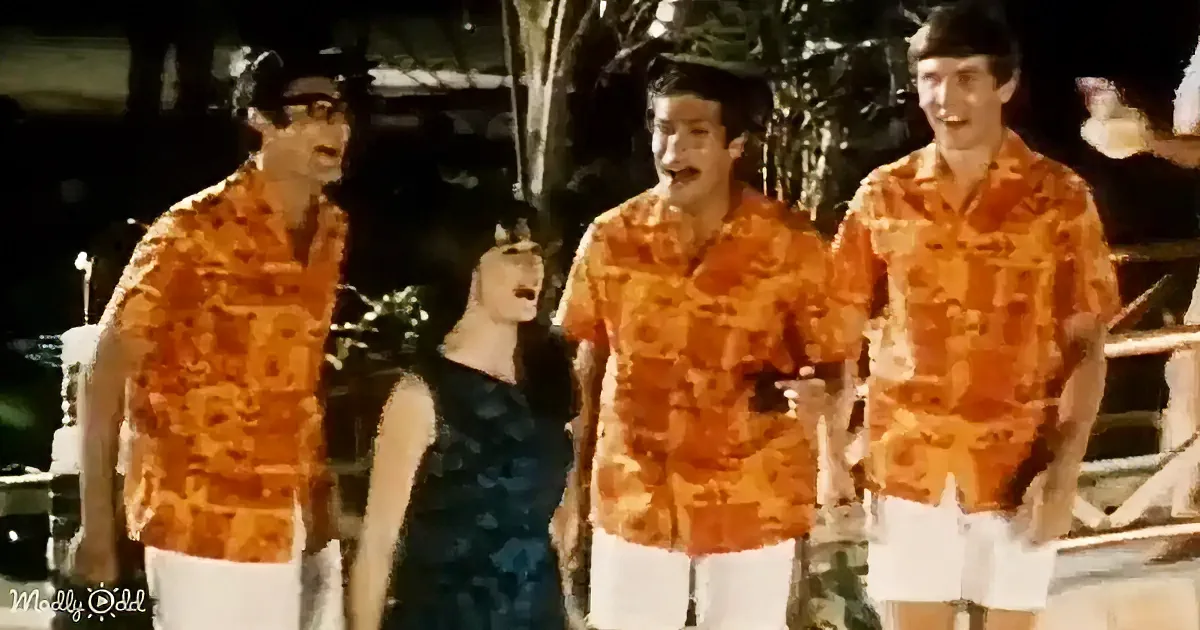 Three men in orange shirts and a woman in a black dress stand together, possibly singing or performing.