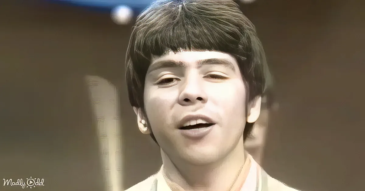 A young person with short dark hair and a light-colored shirt is shown in a close-up, with their mouth slightly open.