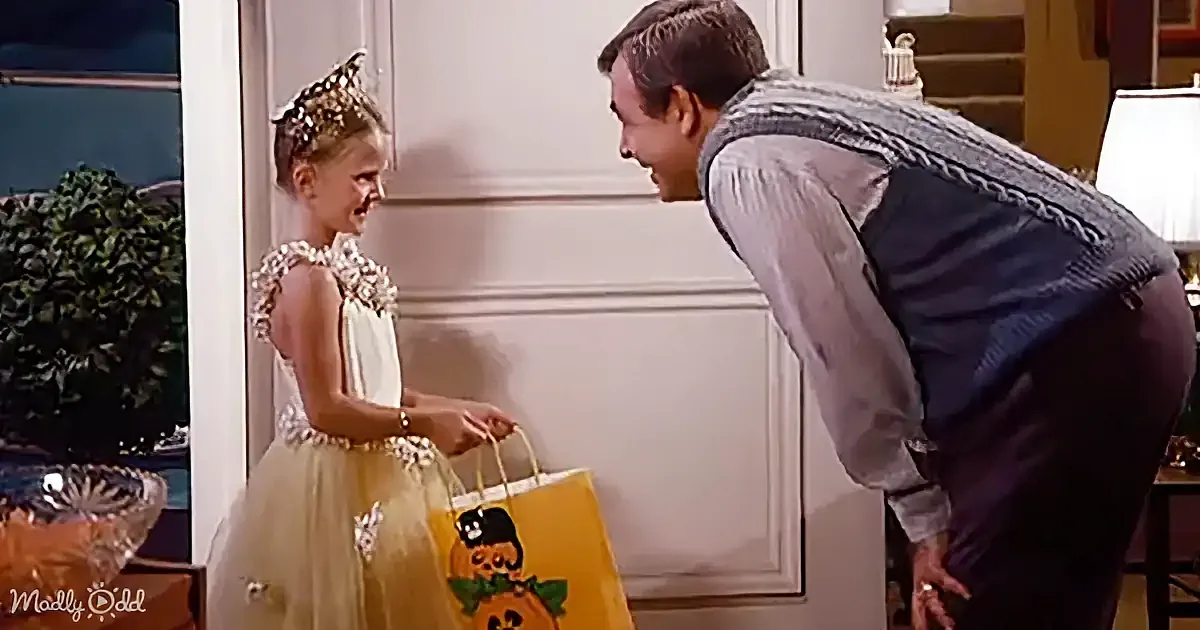 A young girl in a princess costume holds a bag while a man bends down to talk to her.