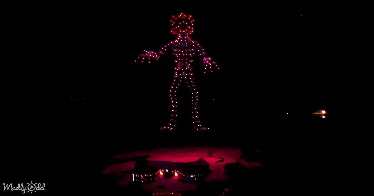 A glowing humanoid figure made of red and purple lights stands against a dark sky, casting a red glow on the ground.