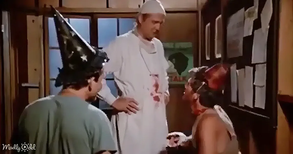 A man in a white lab coat stands between two others, one in a wizard hat and the other in a tank top, in a room with a...