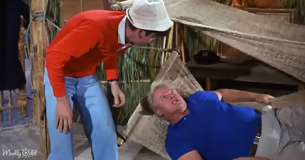 A man in a red shirt and white hat leans over another man in a blue shirt lying on a stone surface.