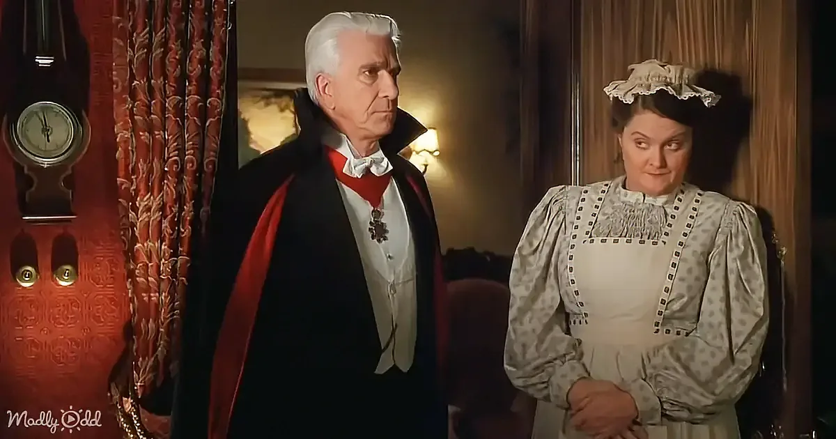 A man in a black coat with a red sash and a woman in a white dress with a lace cap are standing in a dimly lit room.