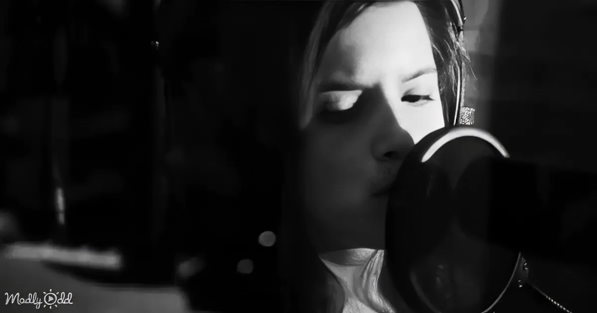 A person wearing headphones is singing into a microphone in a dimly lit room.