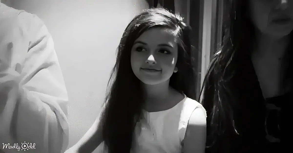 A young girl with long hair, wearing a white top, smiles softly in a black-and-white image.